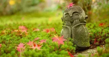 Hoja de arce rojo en la cabeza del pequeño monje budista japonés doll rock en el jardín japonés